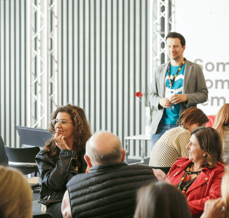 Fotografia de capçalera de la pàgina on es veu un grup de persones assegudes escoltant atentament i somrient